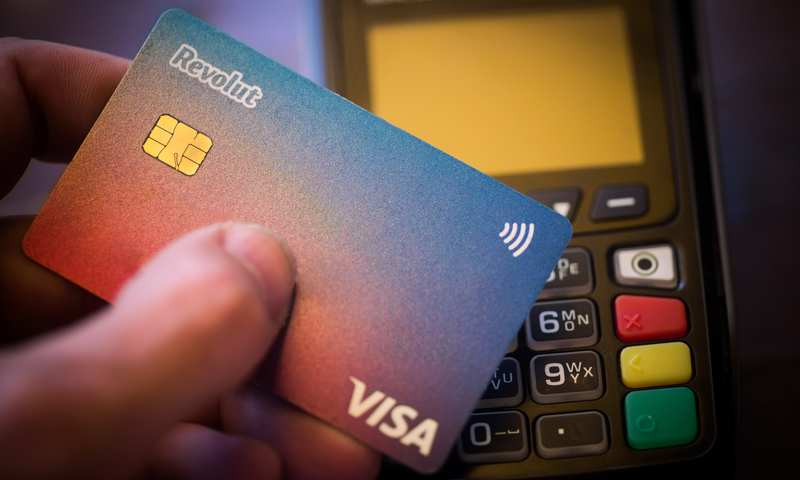 Bucharest, ROMANIA – May 17, 2021: Illustrative editorial concept image of a person holding a Revolut VISA card near a POS terminal.