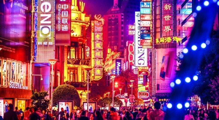 Crowds walk below neon signs on Nanjing Road. The street is the main shopping district of the city and one of the world’s busiest shopping districts.