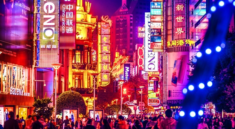 Crowds walk below neon signs on Nanjing Road. The street is the main shopping district of the city and one of the world’s busiest shopping districts.