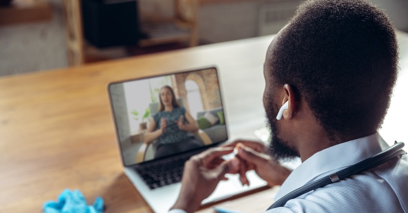 Doctor advising the patient online with laptop. African-american doctor during his work with patients, explaining recipes for drug. Daily hard work for health and lives saving during epidemic.