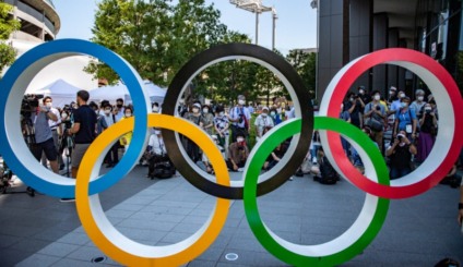People gather near the Olympic Rings to take pictures of the Blue Impulse aerobatic demonstration team of Japan Air Self-Defence Force flying over the Olympic Stadium, the main venue for the Tokyo 2020 Olympic and Paralympic Games, during a rehearsal in Tokyo on July 21, 2021. (Photo by Philip FONG / AFP)