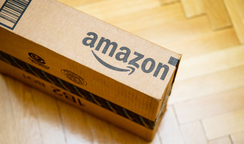 PARIS, FRANCE – JAN 28, 2016: Amazon logotype printed on cardboard box side seen from above on a wooden parwuet floor. Amazon is an American electronic e-commerce company distribution worlwide e-commerce goods