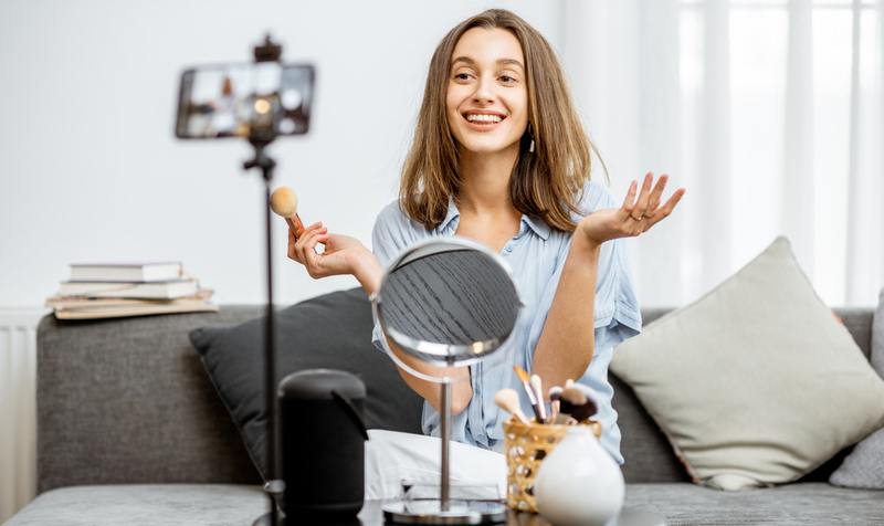 Young woman recording on a smart phone her vlog about cosmetics, showing and demonstrating makeup. Influencer marketing in social media concept