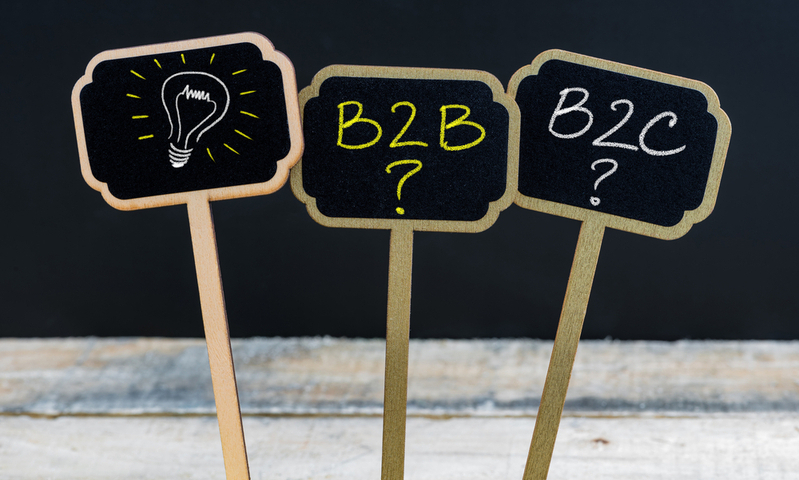 Concept message B2B as Business To Business, B2C as Business To Consumer and light bulb as symbol for idea written with chalk on wooden mini blackboard labels, defocused chalkboard and wood table in background