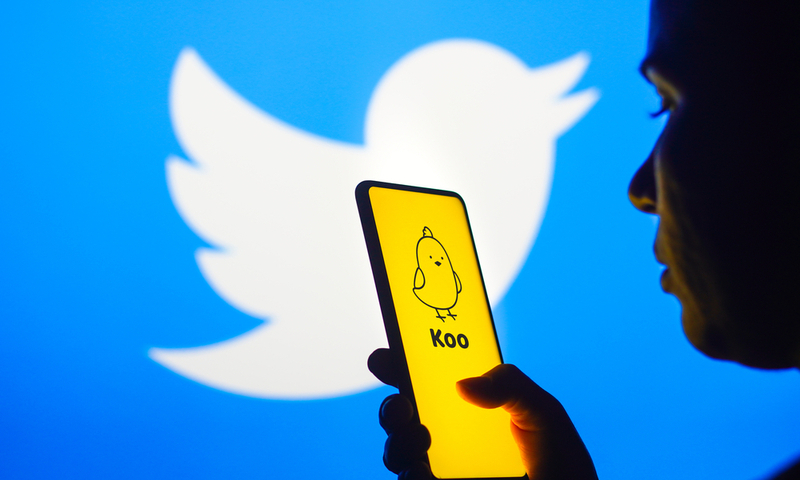 November 18, 2022, Brazil. In this photo illustration, a woman’s silhouette holds a smartphone with an Koo app logo displayed on the screen and the Twitter logo displayed in the background