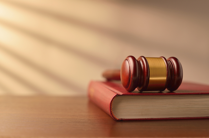 Law book and wooden judges gavel on a wooden table top in a shaft of sunlight with rayed shadow effect, conceptual image of law enforcement with copyspace