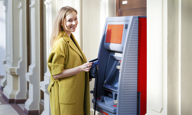 Blonde lady using an automated teller machine . Woman withdrawing money or checking account balance