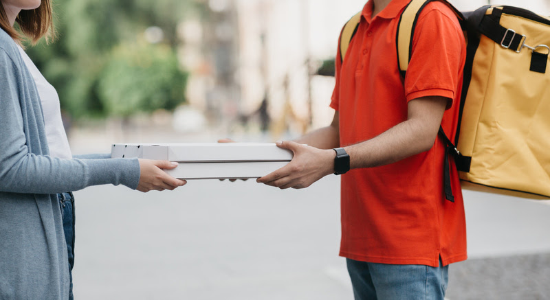 Takeaway and delivery. Delivery man with yellow backpack, smart watches give boxes with pizza for girl in casual on street, side view, panorama, free space