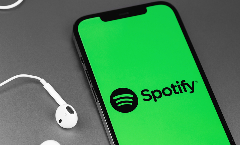 Spotify logo mobile app on screen smartphone iPhone with EarPods headphones closeup. Spotify – online streaming audio service. Moscow, Russia – March 11, 2021