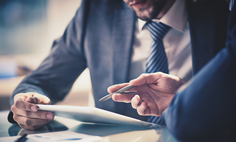 Image of two young businessmen using touchpad at meeting