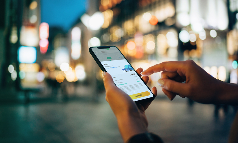 Businesswoman reading financial trading data on smartphone in downtown city street against illuminated urban skyscrapers