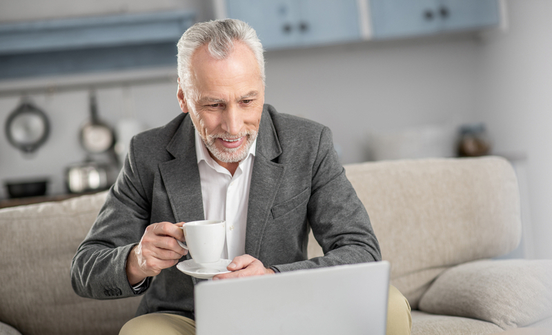 Mature businessman. Cheerful male person being at home and bowing head while staring at his laptop