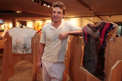 CAssio Reis, na exposição OI T-Shirt, no SPFW, posa ao lado da camistea da Chiara Gadaleta. Foto: Bel Pedrosa/OI