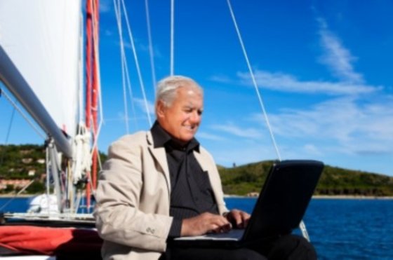 The businessman is working during the vacation on a sailboat with a lovely beach in the background. The businessman is working during the vacation on a sailboat with a lovely beach in the background.