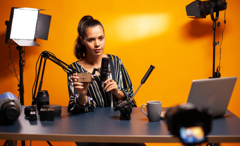 Influencer holding microphone while talking about her vlog equipment. Social media star making online internet content about video equipment for web subscribers and distribution, film