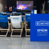 Cadeiras brancas e azuis com o logo da Epson em frente a projeção de um filme oferecido pelo projeto Cinemetrô