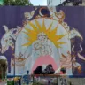 Mural artístico da r.u.a dos amores, em Recife, possui pinturas de mulheres abraçadas, gatos, pássaros, capivara e plantas. As cores roxo e amarelo são predominantes.