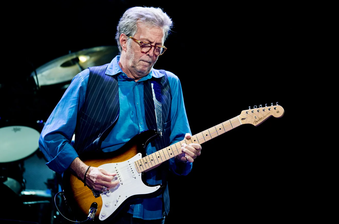 Foto do Eric Clapton no palco da turnê, tocando guitarra