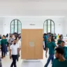 Instalação minimalista traz o logotipo da apple em uma sala branca e está cercada de pessoas