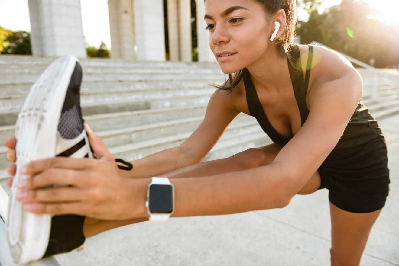 Imagem de uma mulher se alongando para correr, vestindo um smartwatch no pulso