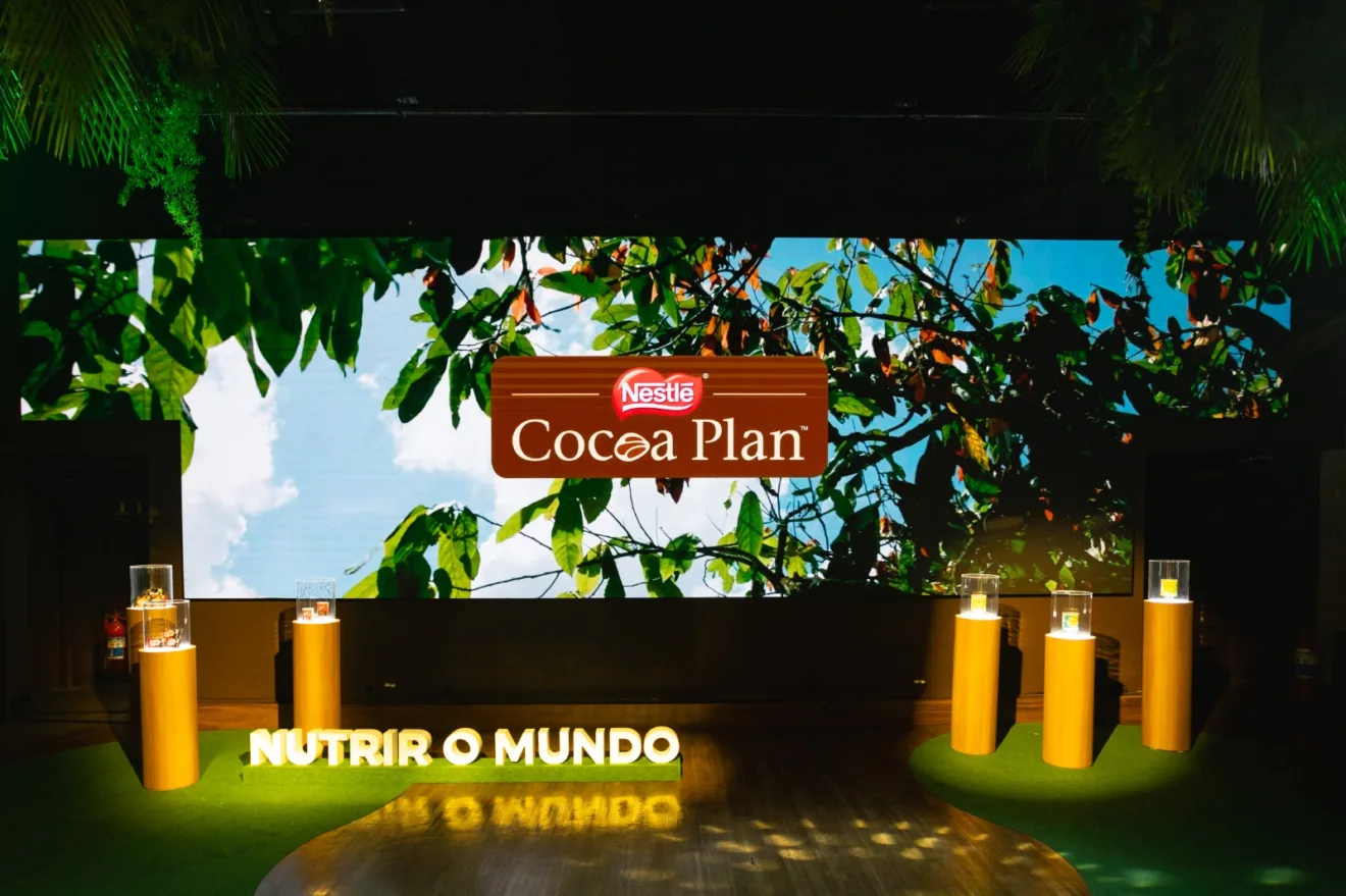 Imagem mostra um palco com a logo de "Cocoa Plan" da Nestlé, e um letreiro escrito "nutrir o mundo"