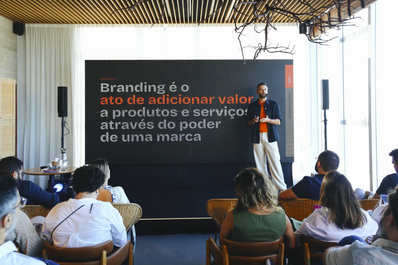 Galileu Nogueira, autor do livro “BDP – Branding de Perto - Um Guia Prático para Construir e Gerenciar sua Marca”, está em pé palestrando no evento da agência Pronto!. No quadro atrás dele, está escrito "Branding é o ato de adicionar valor a produtos e serviços através do poder de uma marca".