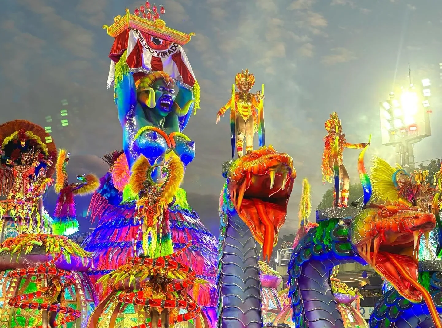 Desfile de Carnaval com cenografia de dragões e criaturas grandes azuis, compondo um cenário colorido