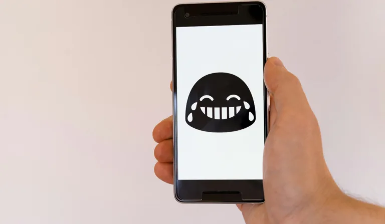 Imagem de um celular com um emoji de risada na tela, simbolizando o Dia da Mentira